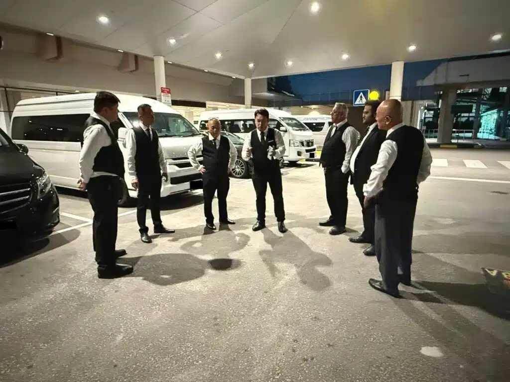A professional team of private drivers in Singapore standing together in uniform near their transport vans at an airport zone.