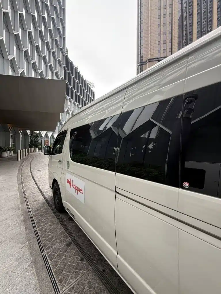 Token2049 Singapore 2026 Side Event Transport with a white Hopper shuttle van parked outside a modern high-rise building.